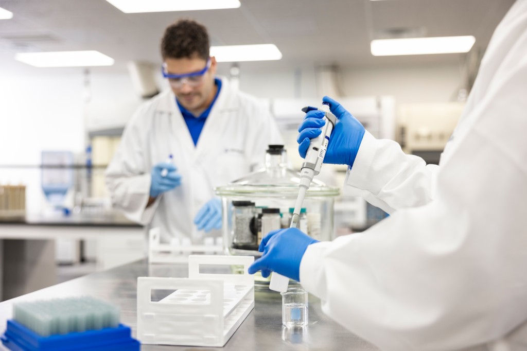 Zwei Laboranten in Schutzkittel und -brille testen auf unbeabsichtigt eingebrachte Stoffe.