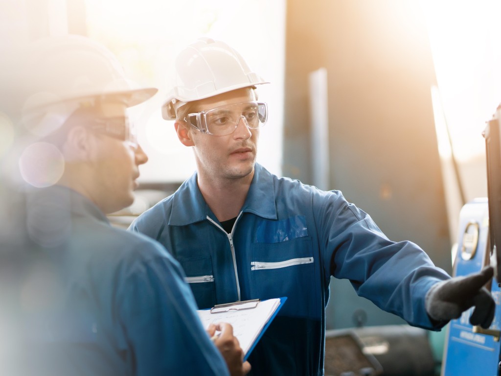 Dos maquinistas con cascos y gafas de protección manipulando una máquina