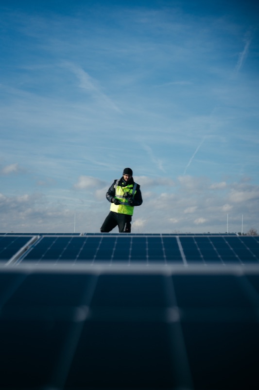 Ingenieur in Sicherheitsweste inmitten von Solarmodulen unter bewölktem Himmel
