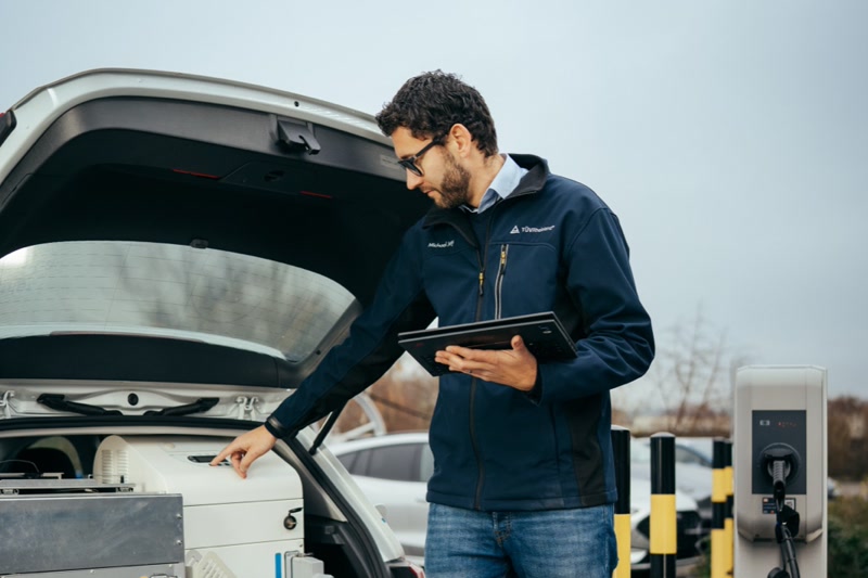 Ingenieur mit Tablet bei der Prüfung eines Elektrofahrzeugs an einer Ladestation