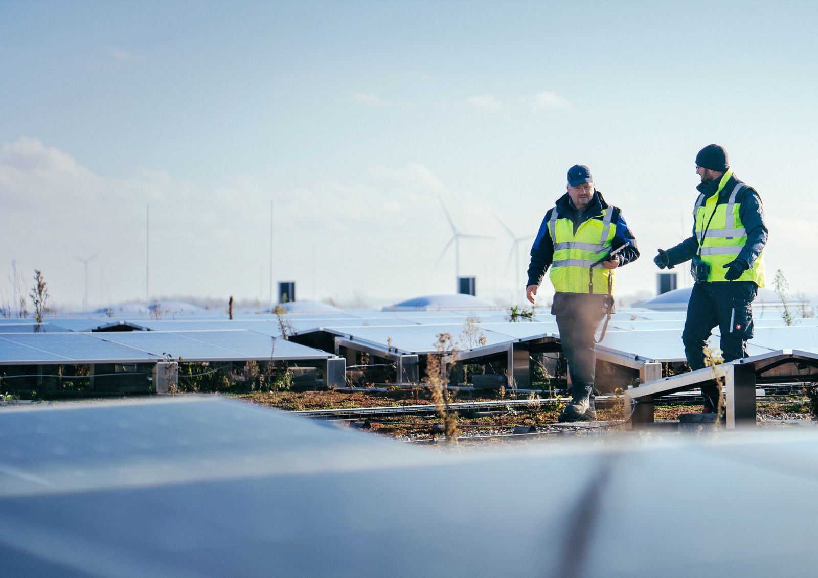Zwei Techniker in Sicherheitswesten bei der Inspektion von Solarmodulen im Winter