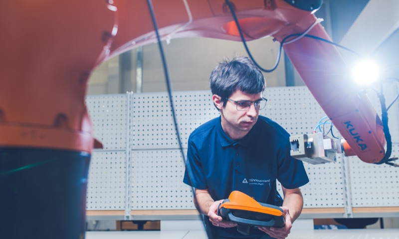 Technician operating a controller near an industrial robotic arm
